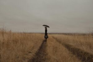 person in black standing alone in a field with an umbrella